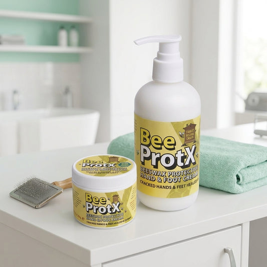 BeeProtX Beeswax Barrier Hand & Foot Cream shown as a large white pump bottle and a smaller matching tub on a white bathroom counter, with a folded mint green towel and a metal brush nearby.