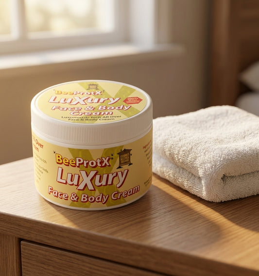 A jar of BeeProtX Luxury Face & Body Cream sits on a light wood bedside table next to a folded white towel, with a softly blurred bedroom background.