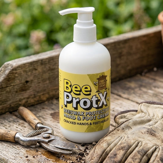 A pumper of BeeProtX Beeswax Hand & Foot cream sits on a rustic wooden workbench surrounded by gardening tools, including pruning shears, gloves, and soil, with a blurred garden background.