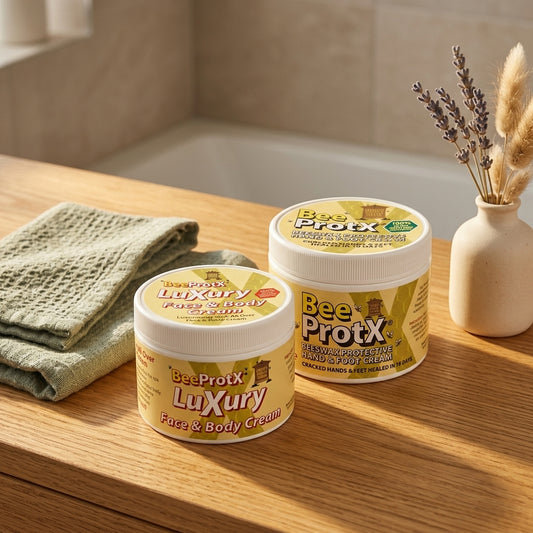 Two jars of BeeProtX Cream are displayed on a wooden bathroom ledge next to a folded green towel and a small vase with dried lavender.