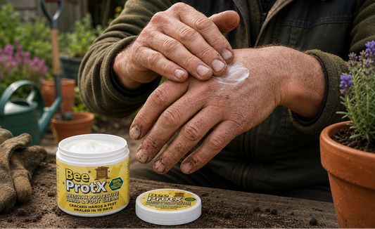 A person outdoors applies a white cream from a jar labeled BeeProtX to their hand. The product jar and lid sit on a wooden surface with gardening tools and potted plants in the background.