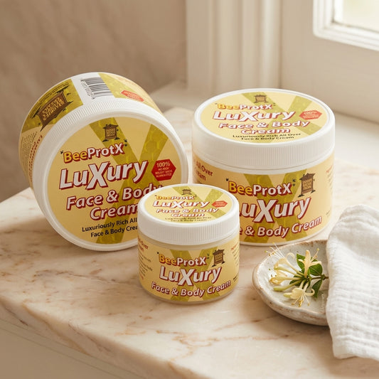 Three jars of BeeProtX Luxury Face & Body Cream arranged on a marble countertop with a folded white towel and small dish of flowers nearby.