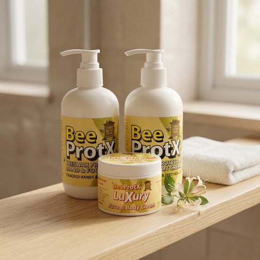 Three BeeProtX skincare products arranged on a wooden shelf in a bright indoor setting: two large pump bottles labeled Hand & Foot Cream and one smaller jar labeled Luxury Face & Body Cream, with a folded white towel and small flowers beside them.