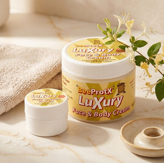 Two jars of BeeProtX Luxury Face & Body Cream on a marble surface with a beige towel, honeycomb dish, and yellow honeysuckle flowers.