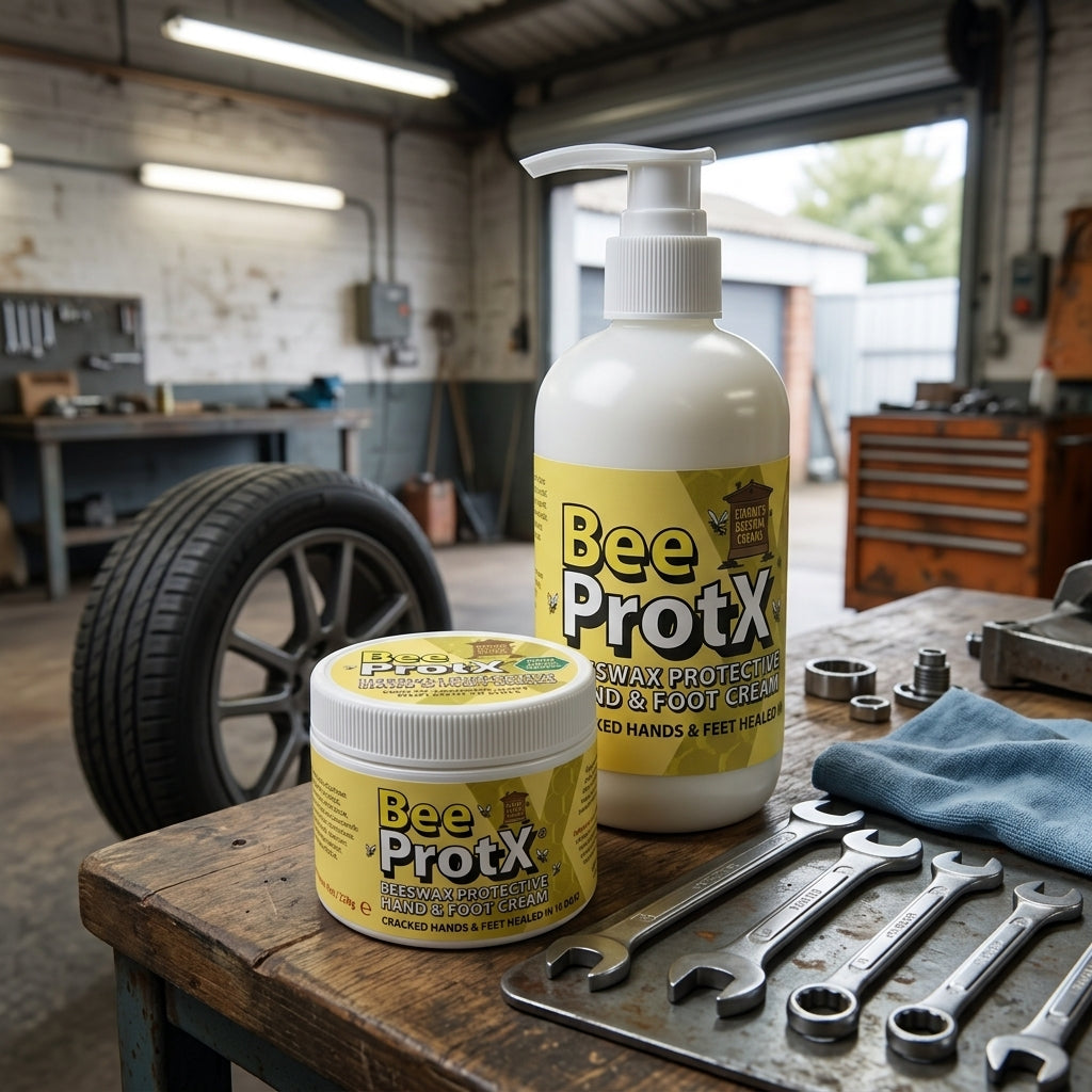 Two jars of BeeProtX Beeswax Barrier Hand and Foot Cream displayed on a rustic workbench inside a garage workshop, with wrenches, a tire, and tools in the background.