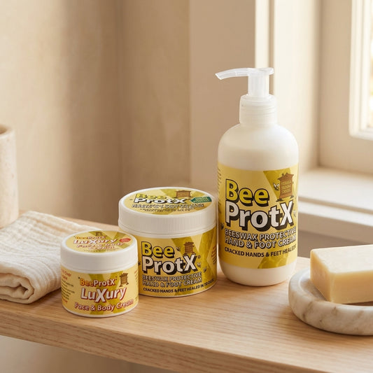 BeeProtX beeswax skincare range — Luxury Face & Body Cream, Hand & Foot Cream tub, and pump bottle, displayed on a wooden shelf with a folded towel and soap dish.