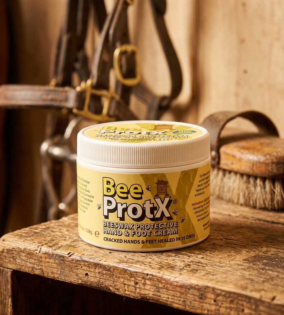 A jar of BeeProtX Beeswax Protective Hand & Foot Cream sits on a rustic wooden table, with equestrian tack blurred in the background.