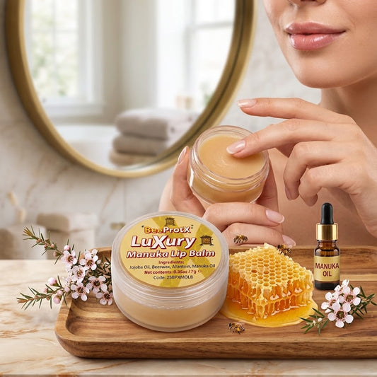 A woman holds an open jar of Luxury BeeProtX Manuka Lip Balm, with the product jar and a small bottle of Manuka Oil arranged on a wooden tray with honeycomb and flowers in a bright bathroom setting.
