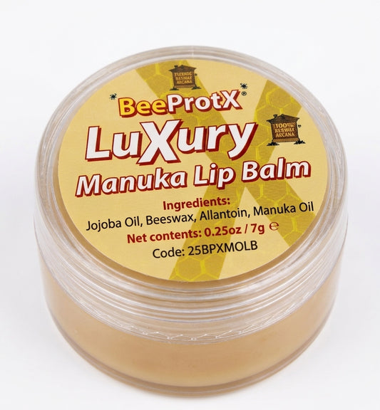 A round clear plastic jar of BeeProtX Luxury Manuka Lip Balm, showing the light tan balm inside and a yellow label with red and white text.