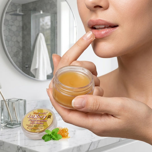 A close-up of a woman applying BeeProtX lip balm from a small clear jar to her lips in a bright bathroom setting. The jar and its lid are shown on a marble counter, with a round mirror and toiletries in the background.